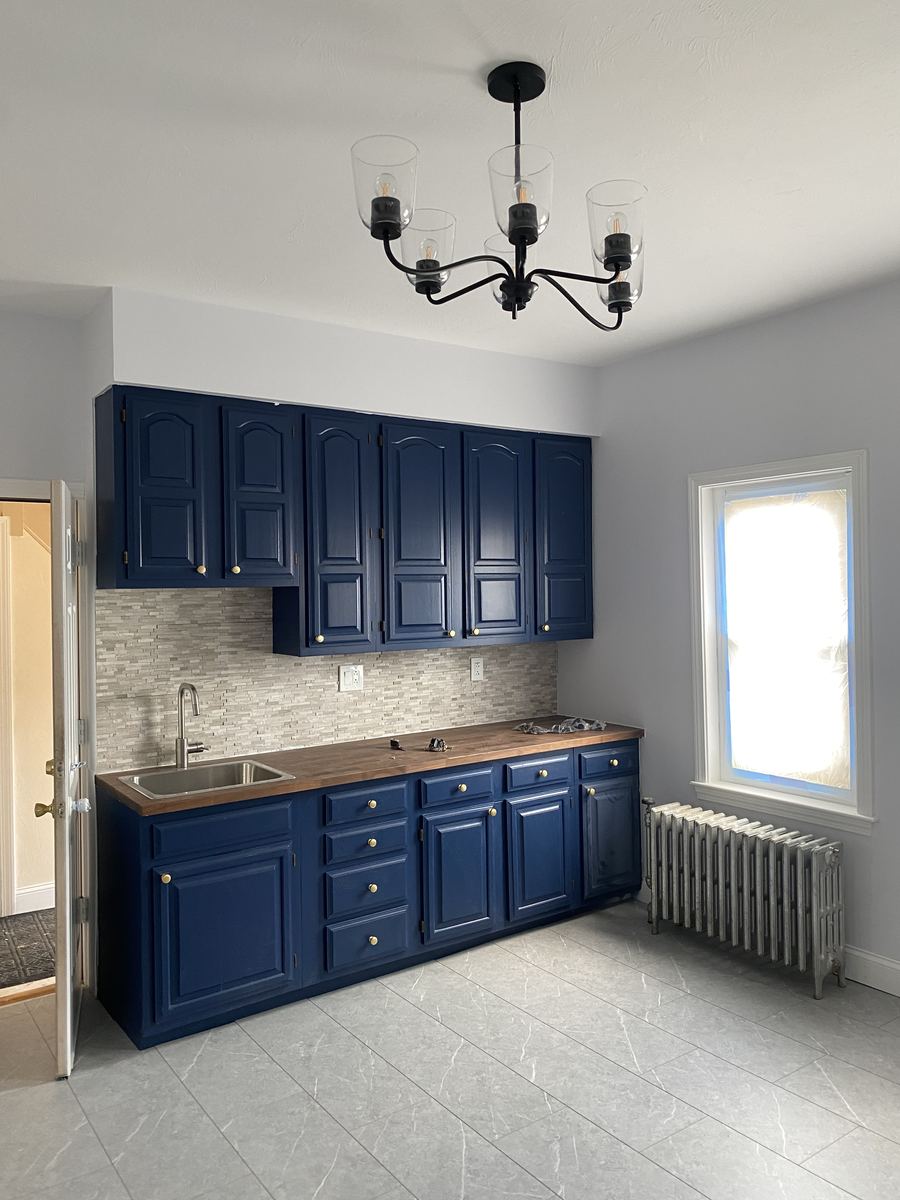 Finished kitchen renovation with navy cabinets, butcher block counters, and new lighting